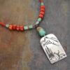 Handcrafted in Colorado, captures the rugged beauty of the Rocky Mountains. with this beaded coral and turquoise necklace. Red beaded necklace with turquoise and coral beads and a silver pewter pendat with mountain and a elk scene